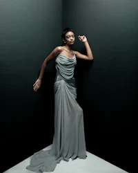 a black woman in a grey gown leaning against a wall